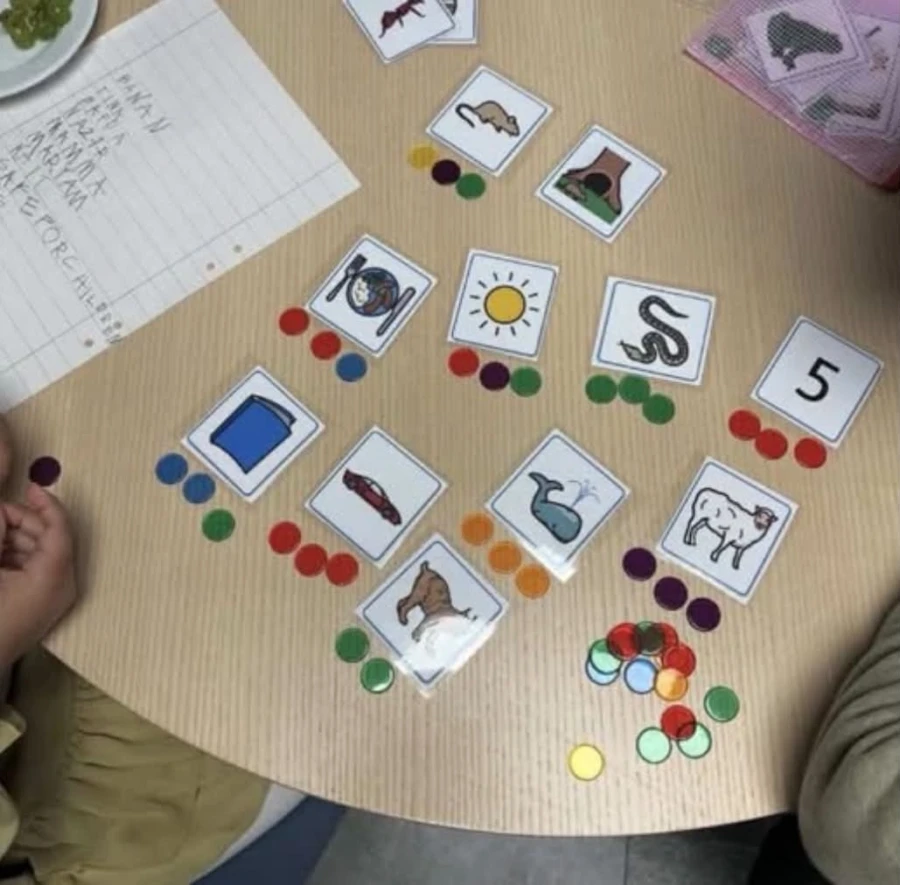 Ett bord med olika bildkort och färgglada spelpjäser används i en interaktiv läsaktivitet för att stimulera barnens intresse för läsning.