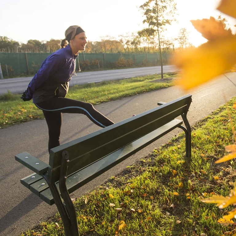 Joggande kvinna som stretchar mot bänk.