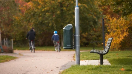 Två cyklister på cykelväg med papperskorg i förgrunden.