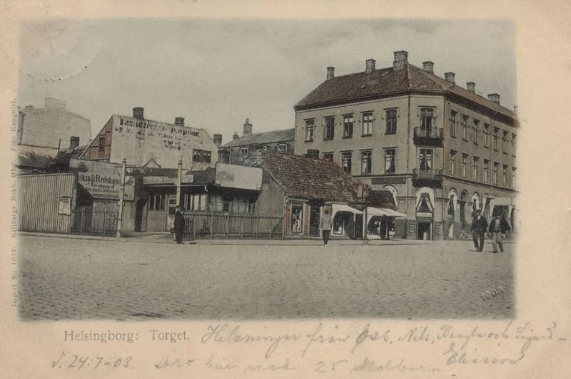 Svartvitt foto med trevåningsbyggna och en låg byggnad bredvid.
