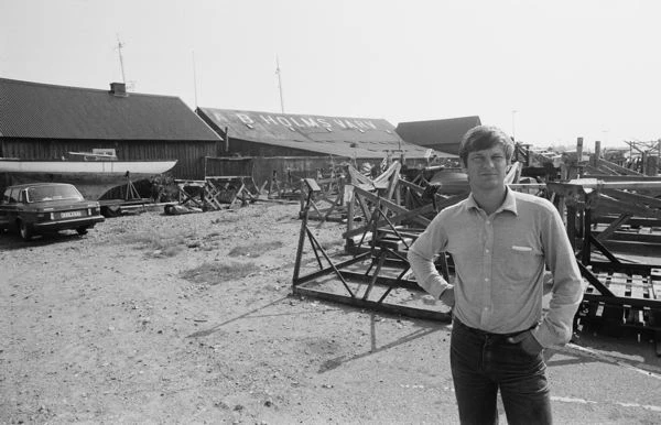 Svartvitt foto på man som står framför frabriksbyggnad.