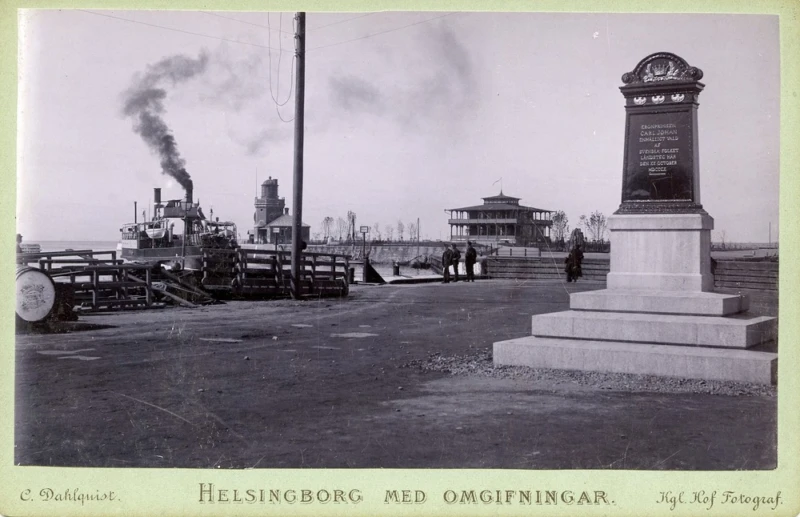 Svartvitt foto på hamn, monument och båt. 