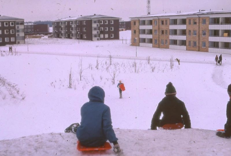 Vinter med flerfamiljshus och barn som åker pulka.