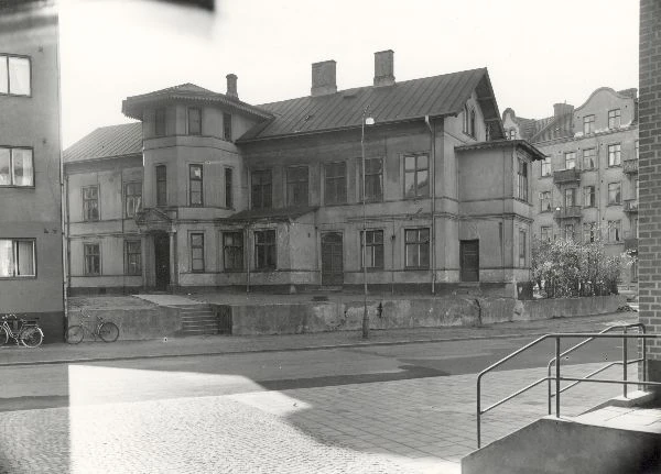 Svartvitt foto, gammal byggnad omgiven av flerfamiljshus. 