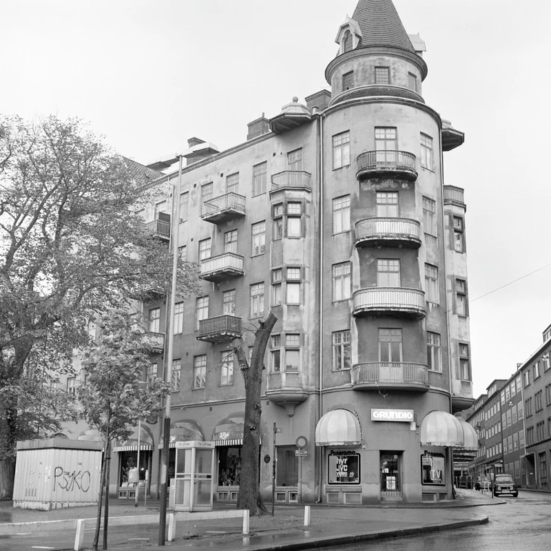 Svartvit bild med hörnbyggnad i sex våningar och ett torn överst.