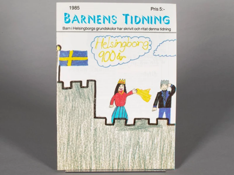 Färgfoto på tidning där det står Helsingborg 900 år" och ett barn har ritat Kärnan och två figurer. 