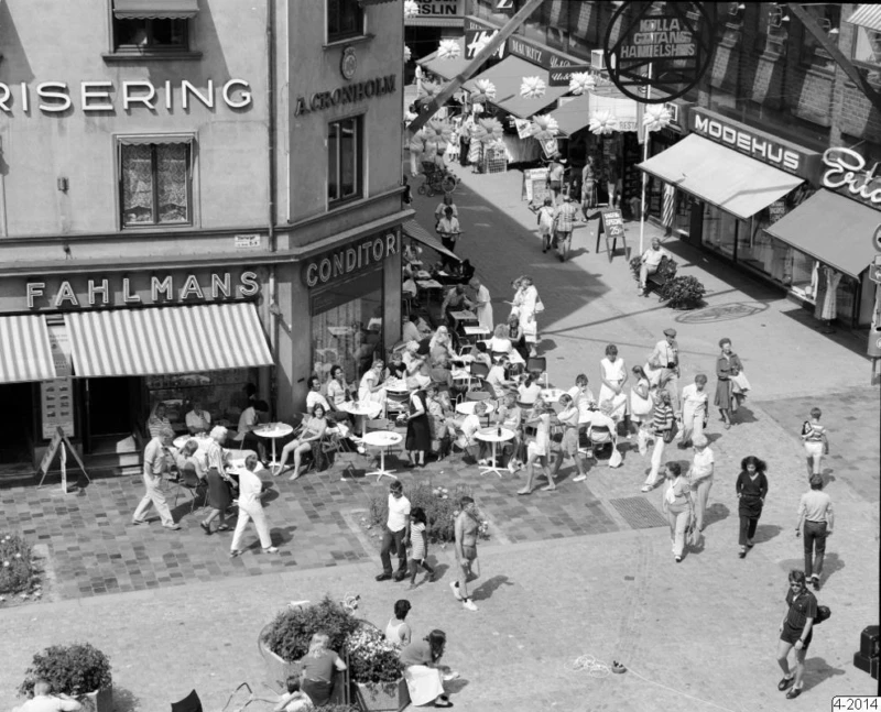 Utomhusbild på Fahlmans gathörn men människor som fikar eller går förbi. Svartvit bild. 