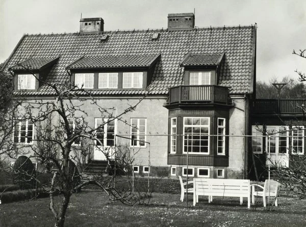 Svartvitt foto på tvåvåningshus och trädgård. 
