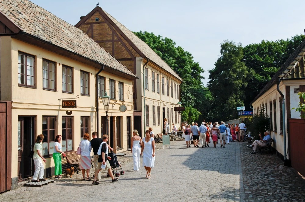 Sommarvy över gammaldags stadsgata med flanerande folk.