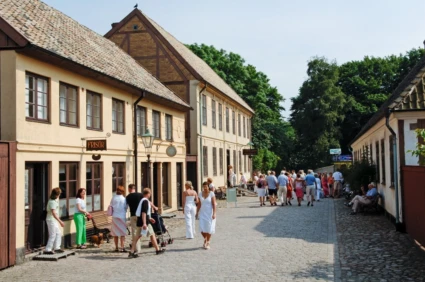 Sommarvy över gammaldags stadsgata med flanerande folk.