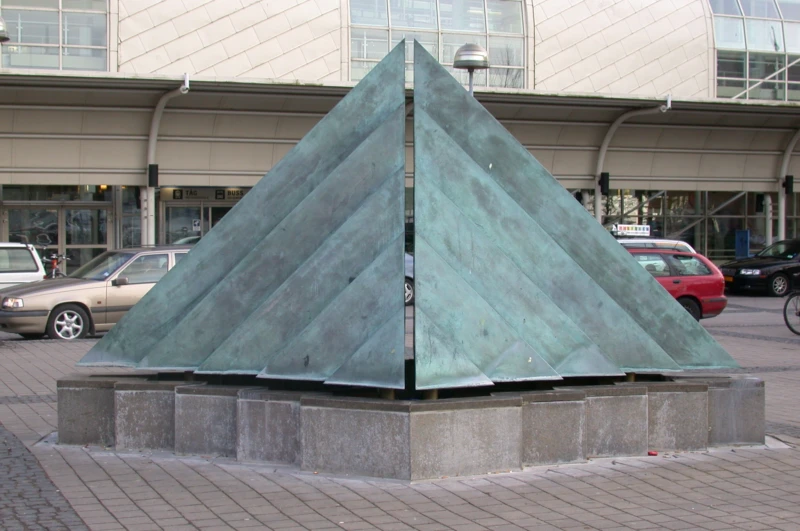 Färgfoto på trekantig bronsskulptur. 