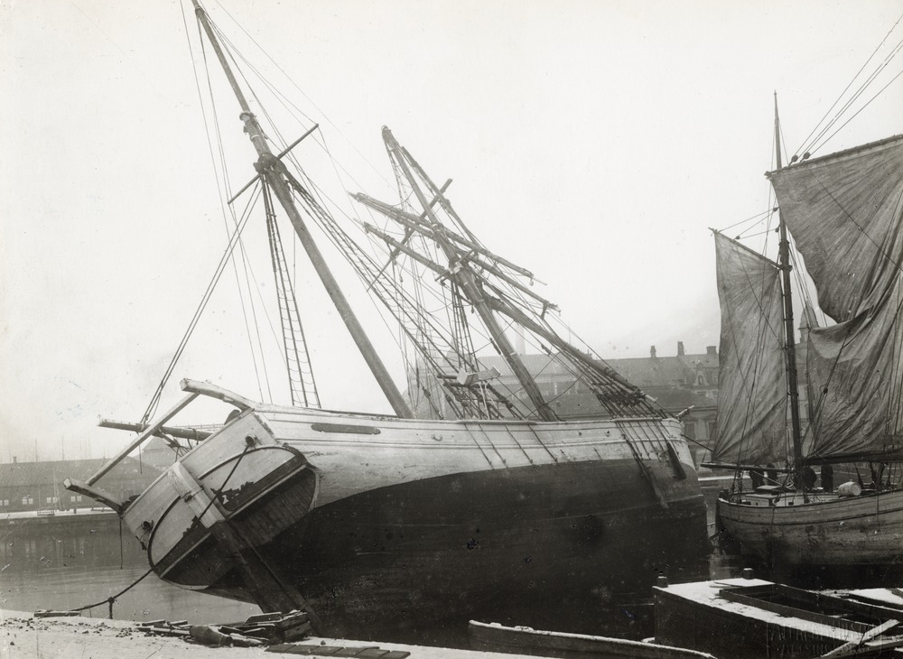 En segelbåt ligger på sidan på land i hamnen efter julstormen 1902.