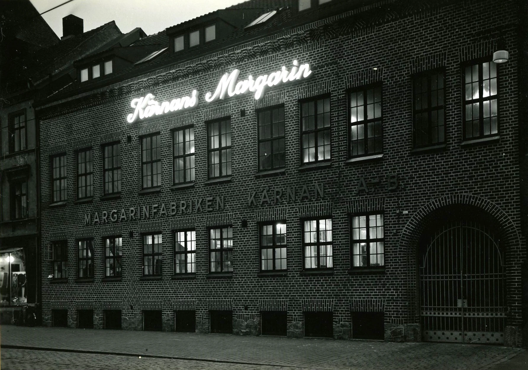 Margarinfabriken Kärnan ABs upplysta fasad kvällstid. Adress: Södergatan 82. Fotograf: Tönnessen. Fotot tillhör Jan Sendelius.