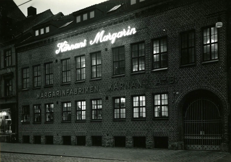 Margarinfabriken Kärnan ABs upplysta fasad kvällstid. Adress: Södergatan 82. Fotograf: Tönnessen. Fotot tillhör Jan Sendelius.