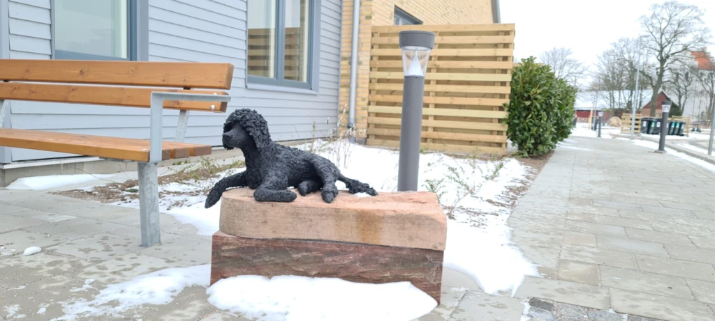 Skulptur av en pudel som ligger på en stensockel.