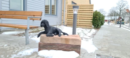 Skulptur av en pudel som ligger på en stensockel.