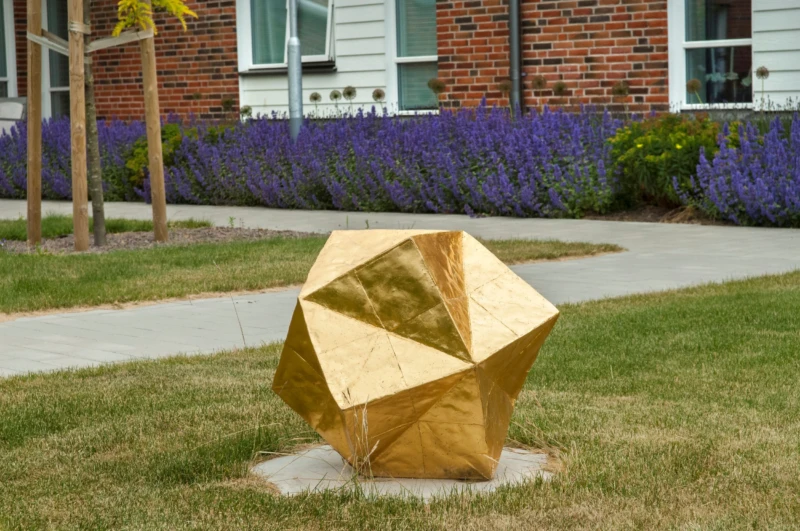Konstverk: förgyllt klot på gräsmattan. 