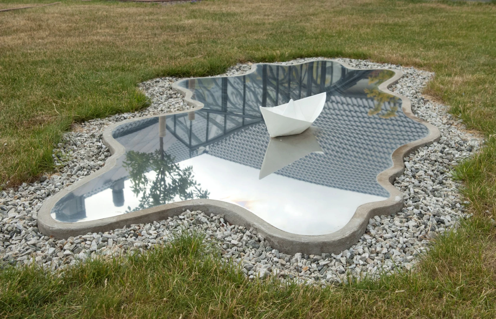 Konstverk på gräset som ser ut som en sjö med en pappersbåt.