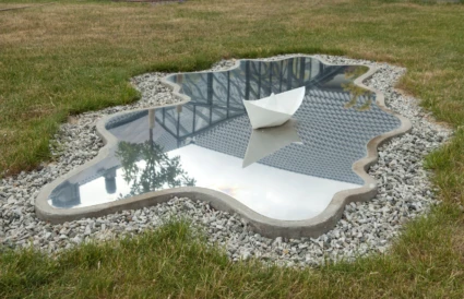 Konstverk på gräset som ser ut som en sjö med en pappersbåt.