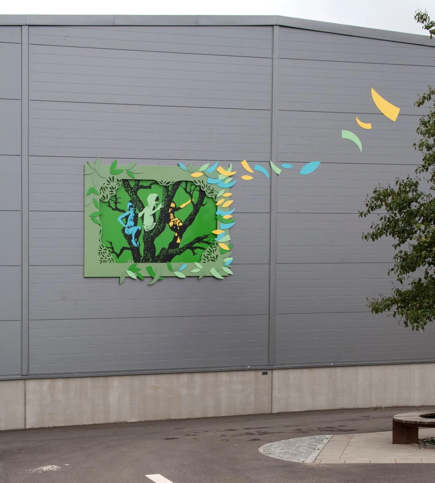 Konstverk på fasad som visar barn som leker i ett träd.