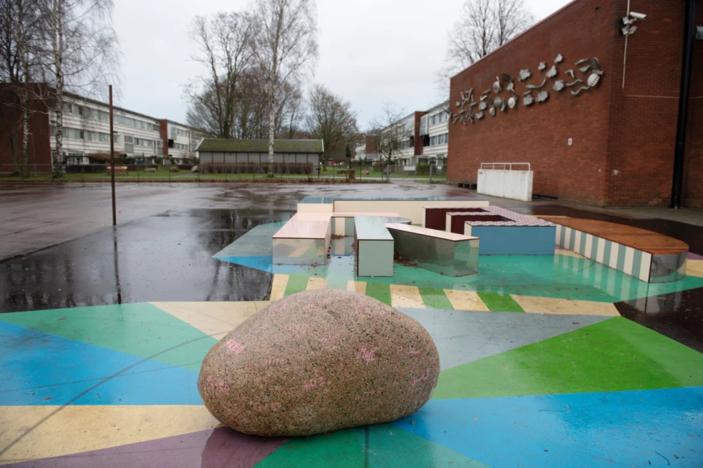 Konstverk utomhus med en sten i förgrunden och glada färger på marken.
