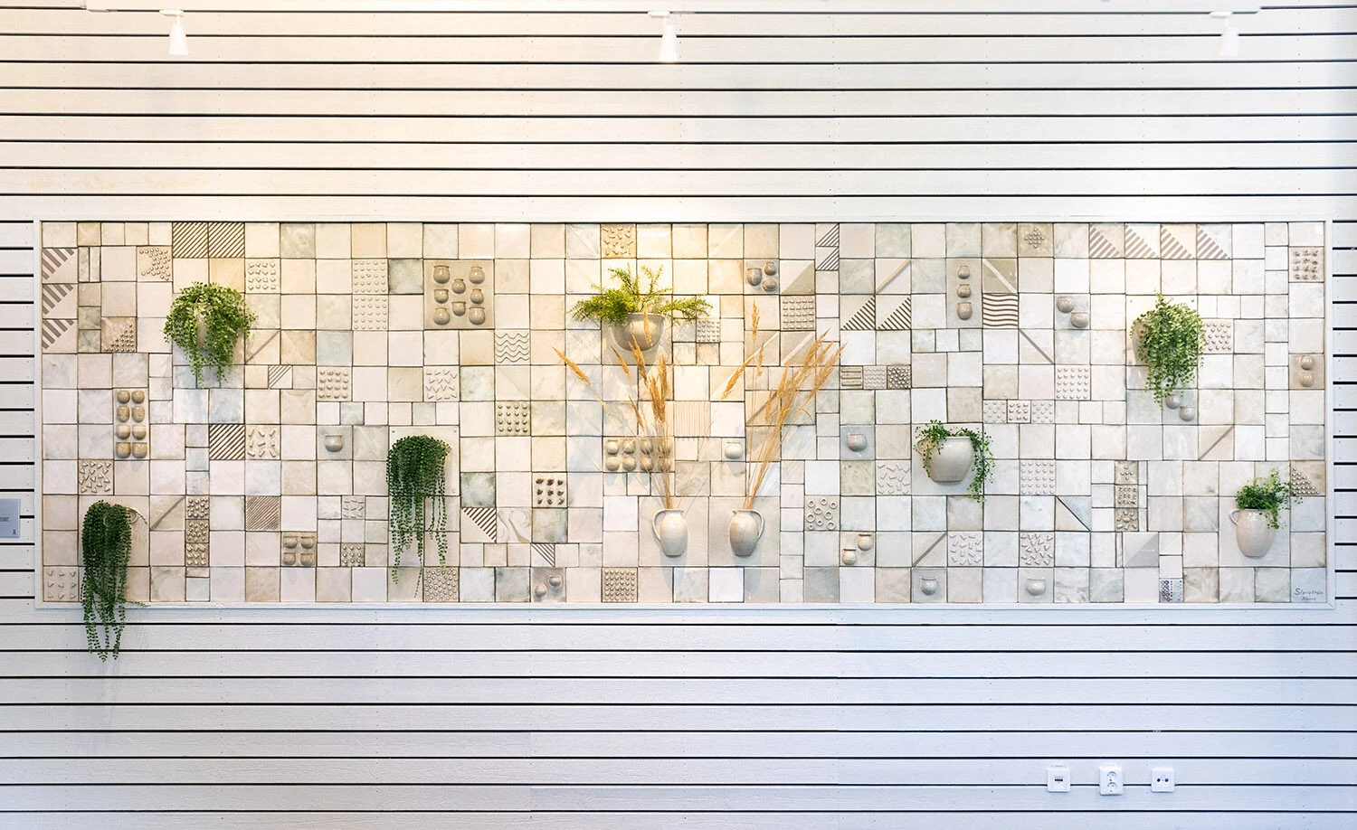 Konstverk på vägg i form av ljusa keramikplattor och halva keramikkärl.