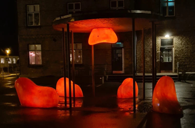 Orangea amorfa ljusskulpturer i mörker på skolgård