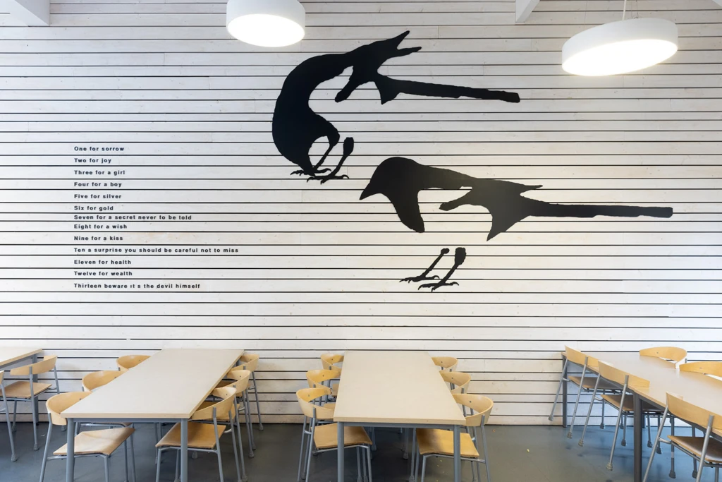 Konstverk på vägg med siluett av skator och text.