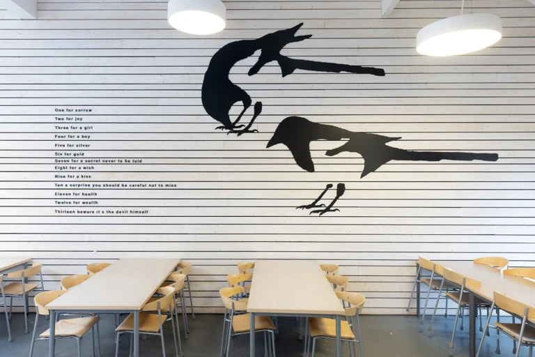 Konstverk på vägg med siluett av skator och text.