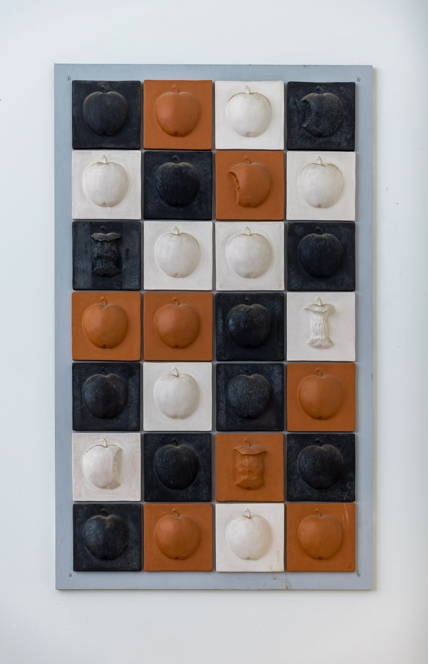 Konstverk av olikfärgade keramikplattor (svart, vit, terracotta) med äppelformer på.