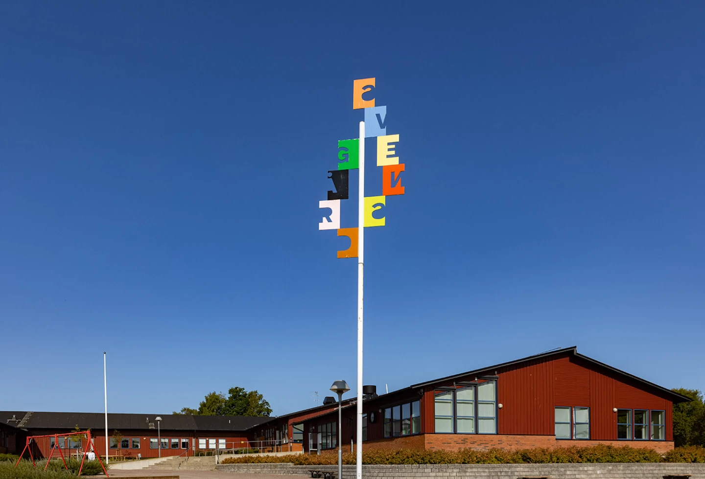 Konstverk i form av en bokstäver på flaggstång som bildar skolans namn.