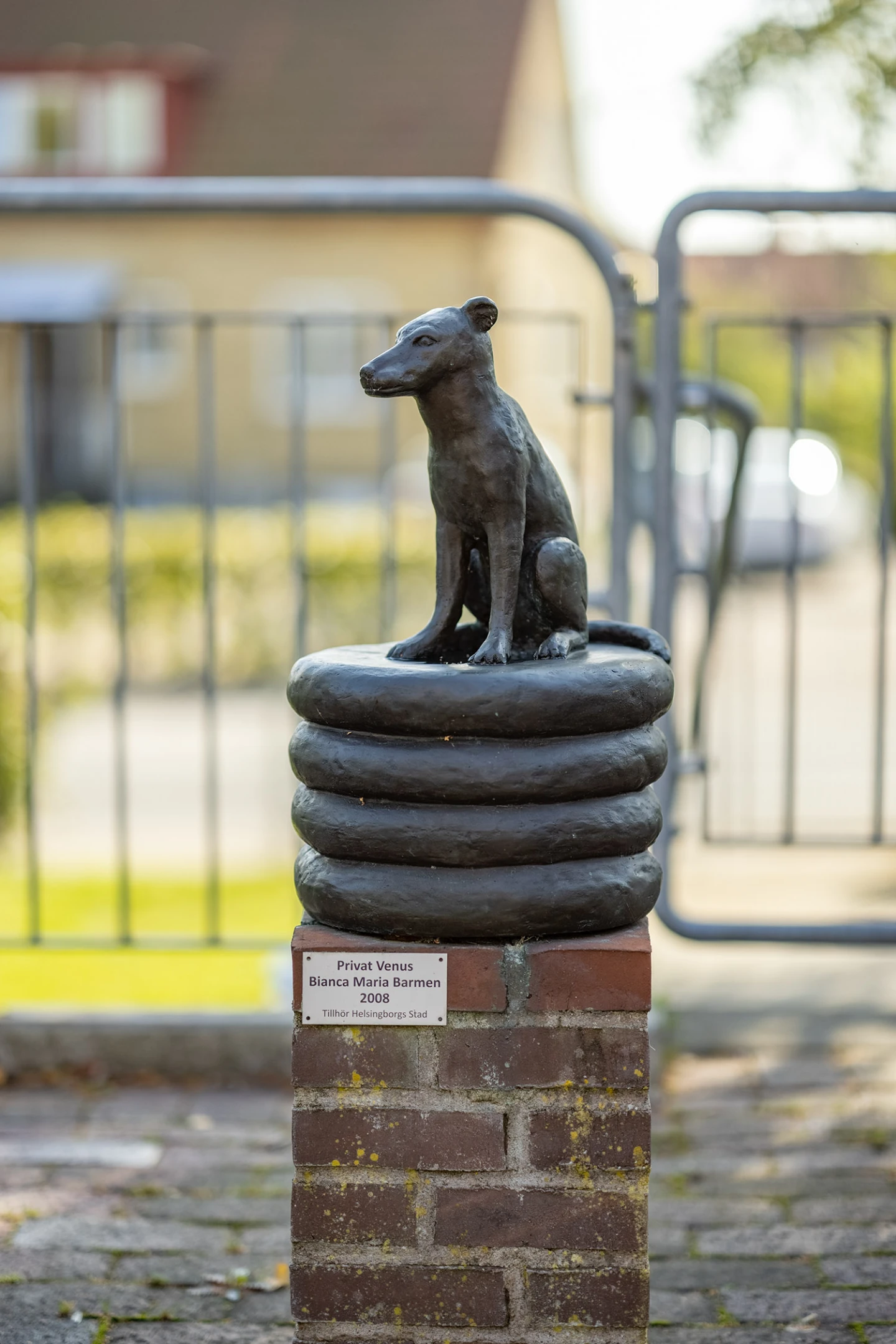 Skulptur som visar en hund sittande på en rund, platt form.
