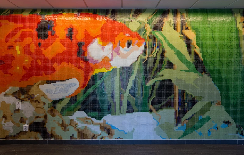 Konstverk på vägg inne och ute i forma av en mosaik av en guldfisk. 