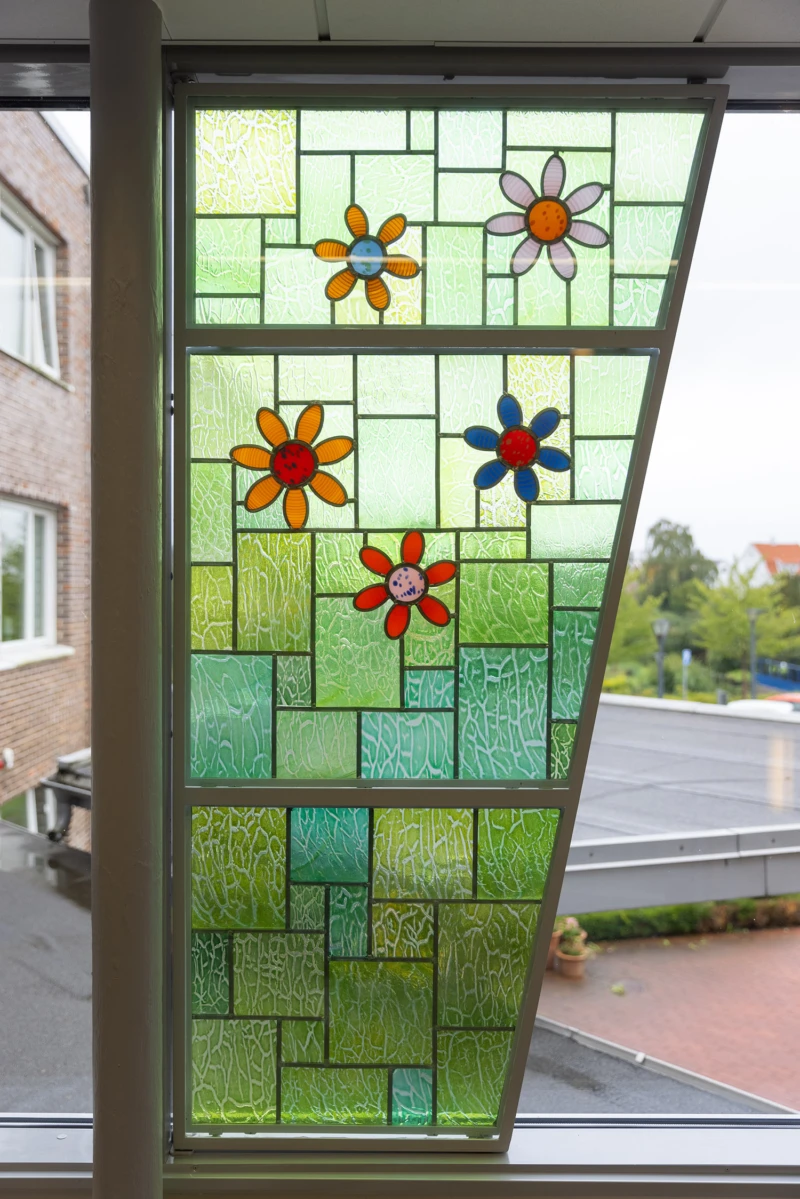 Konstverk i form av glaspanel med motiv av blommor på grönt gräs.