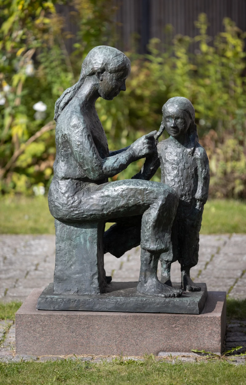 Skulptur som visar två barn, den ena flätar den andras hår.