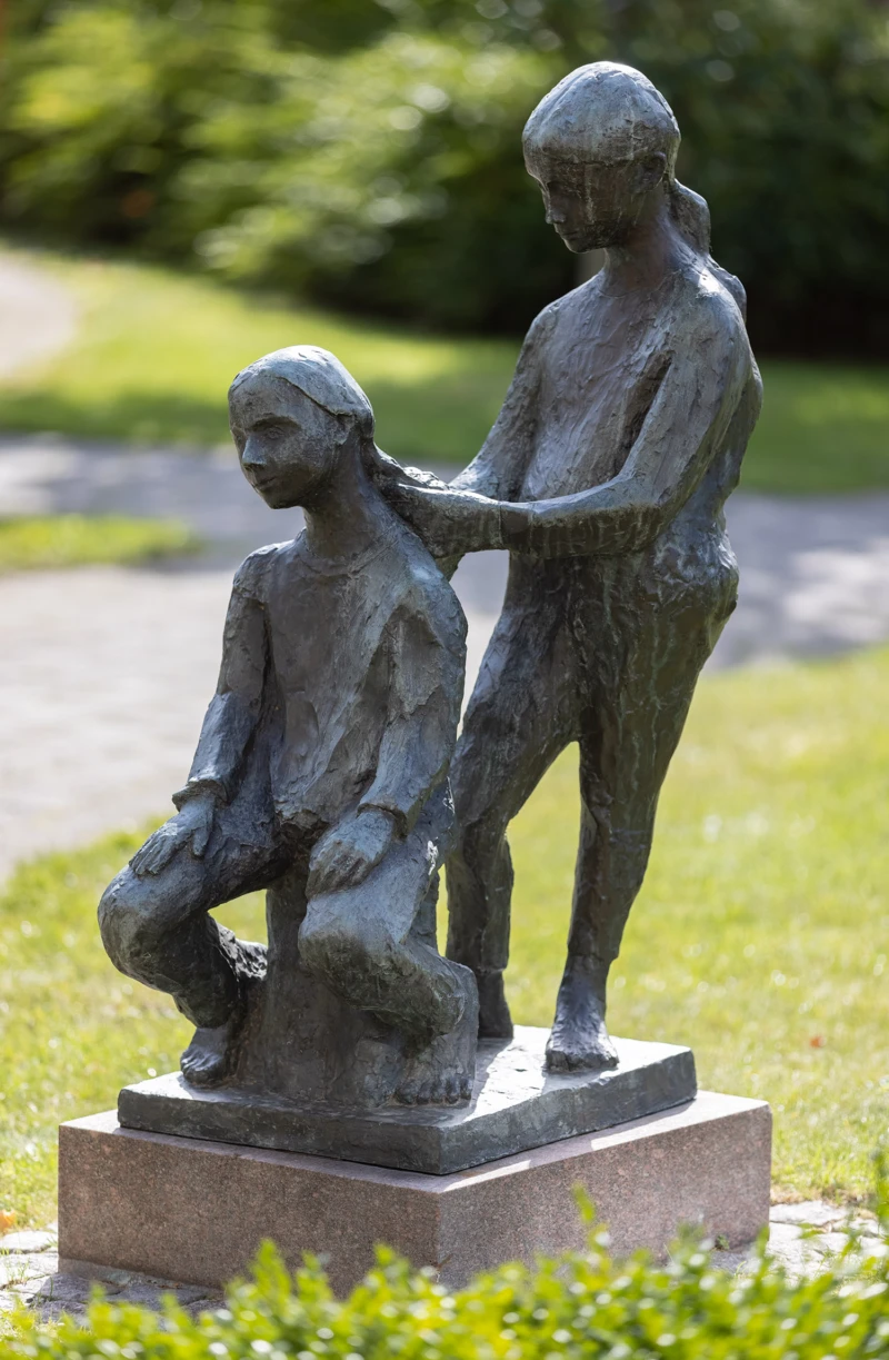 Skulptur som visar två barn, den ena flätar den andras hår. 