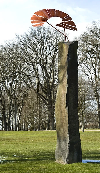 Skulptur med en hög pelare krönt av en röd, abstrakt form.
