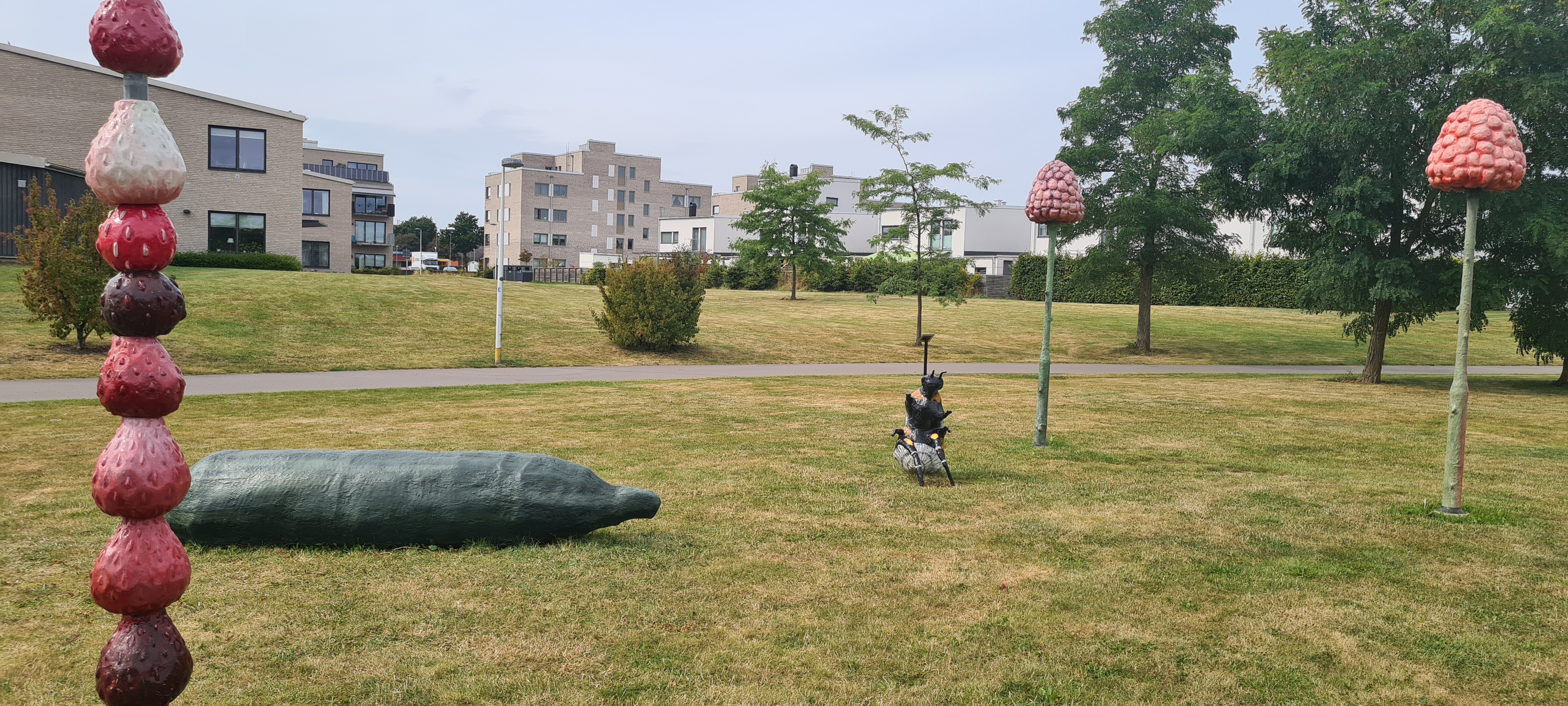 Skulpturer på gräsmatta i form av hallon, gurka, humla och smultron på strå.