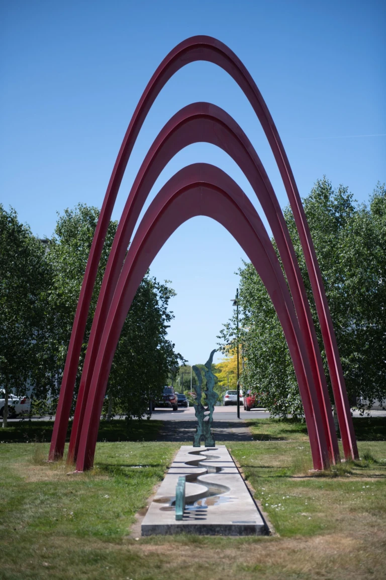 Konstnärlig gestaltning med tre höga röda bågar, en siluett av vintergatan och en slingrande damm.