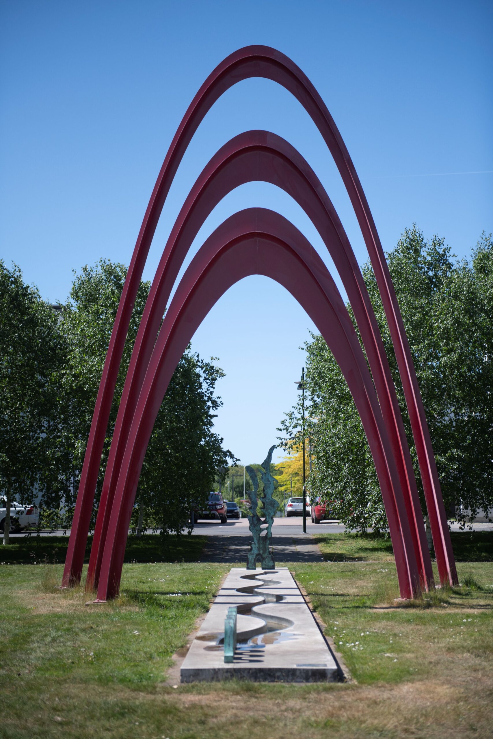 Konstnärlig gestaltning med tre höga röda bågar, en siluett av vintergatan och en slingrande damm.