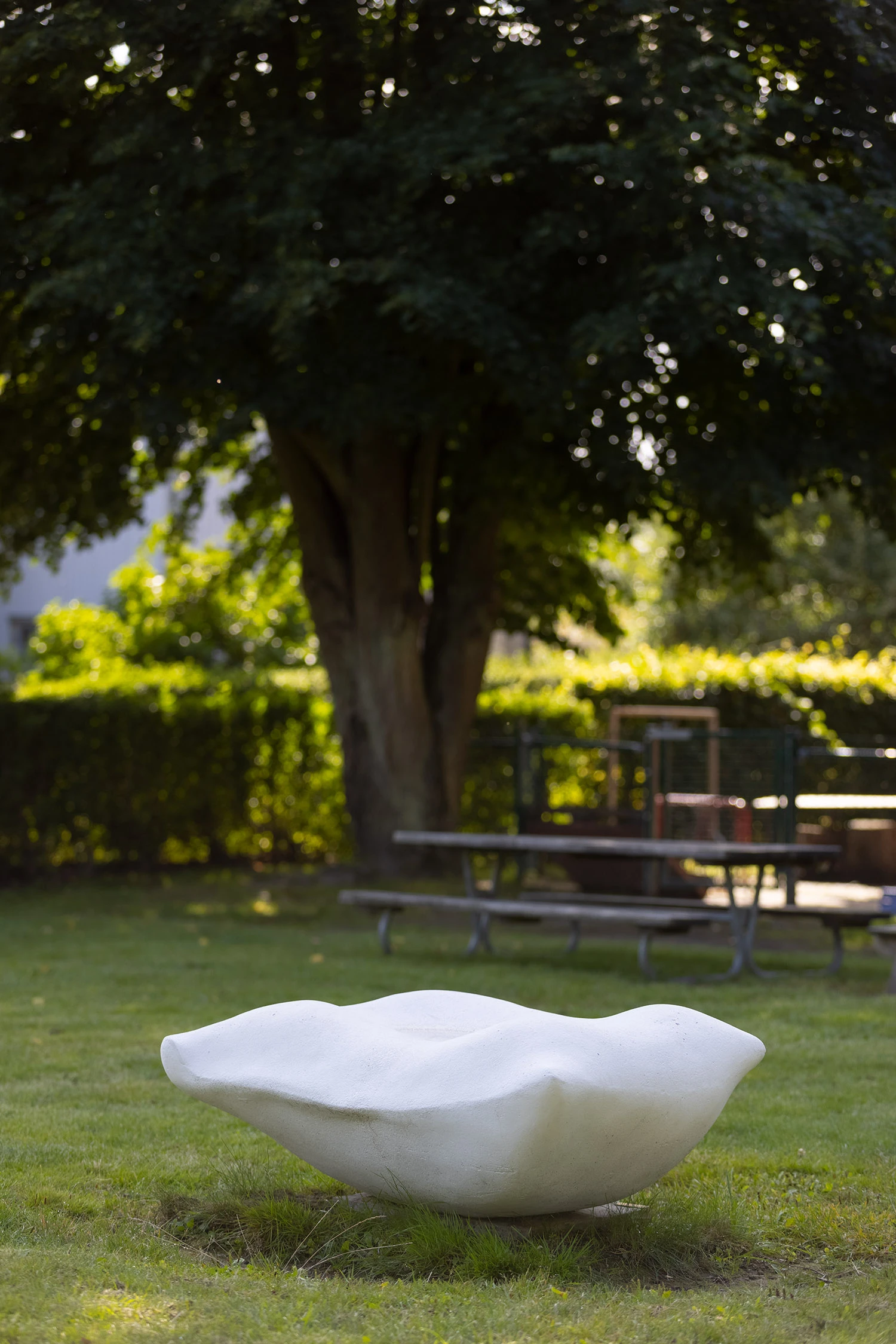 Bild av en vit kudde gjuten i betong. Placerad i en trädgård.