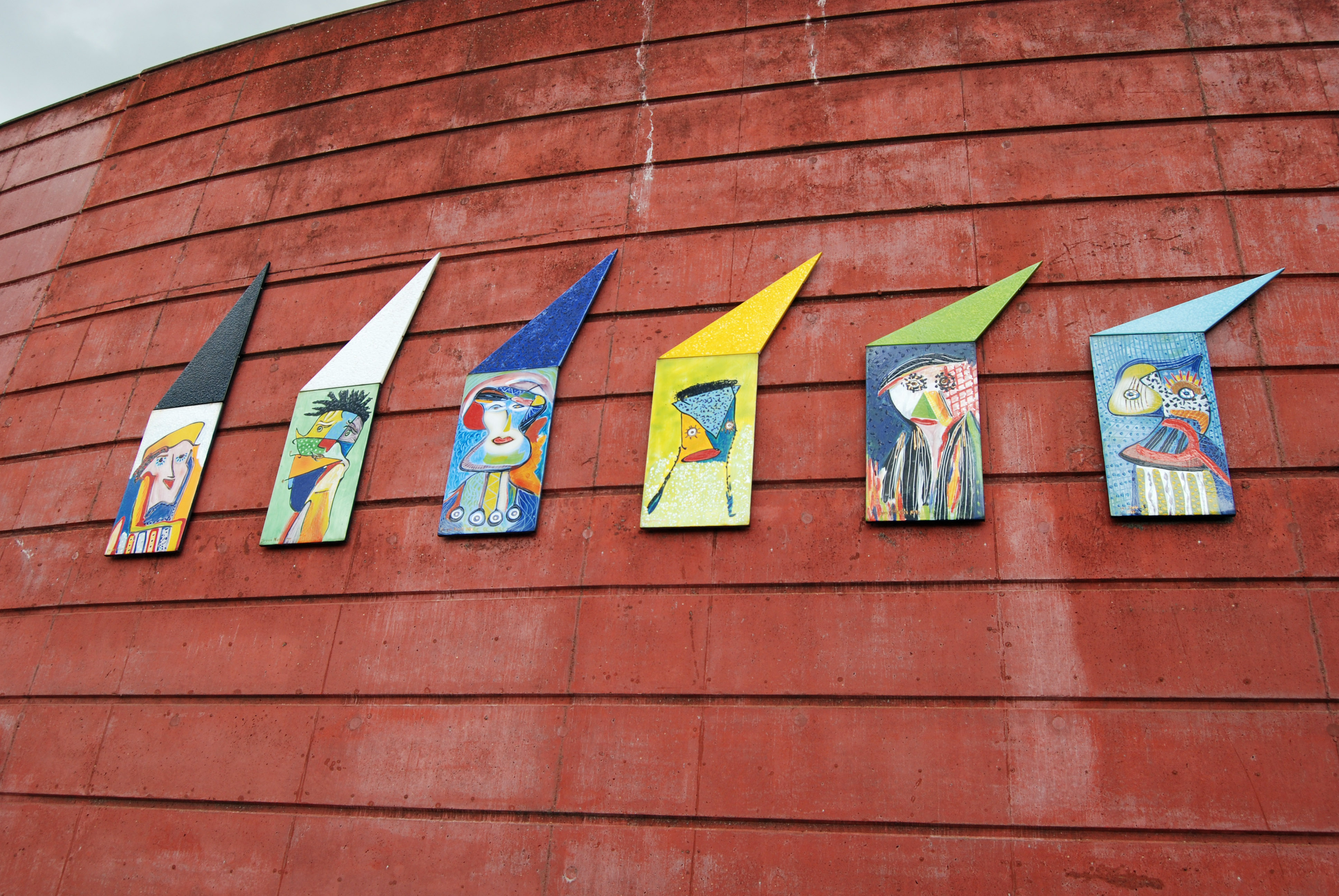 Konstverk på röd betongvägg, sex emaljporträtt i starka färger. 