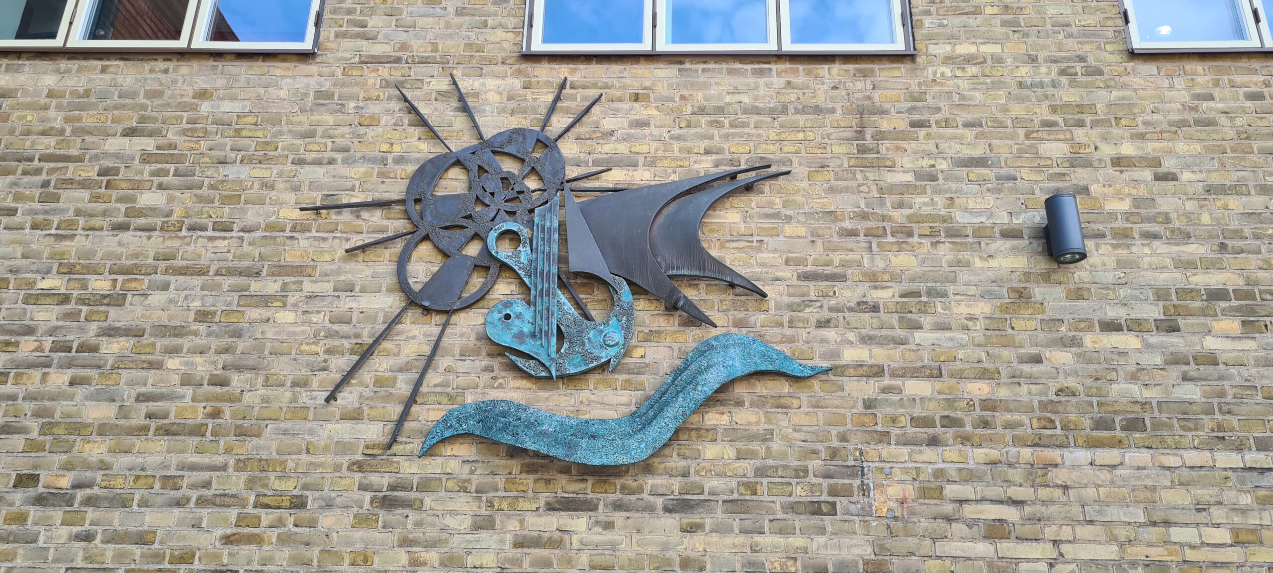 Konstverk i metall på tegelvägg. Mjuka former som bildar sol, segel, vatten ankare och hjärta.
