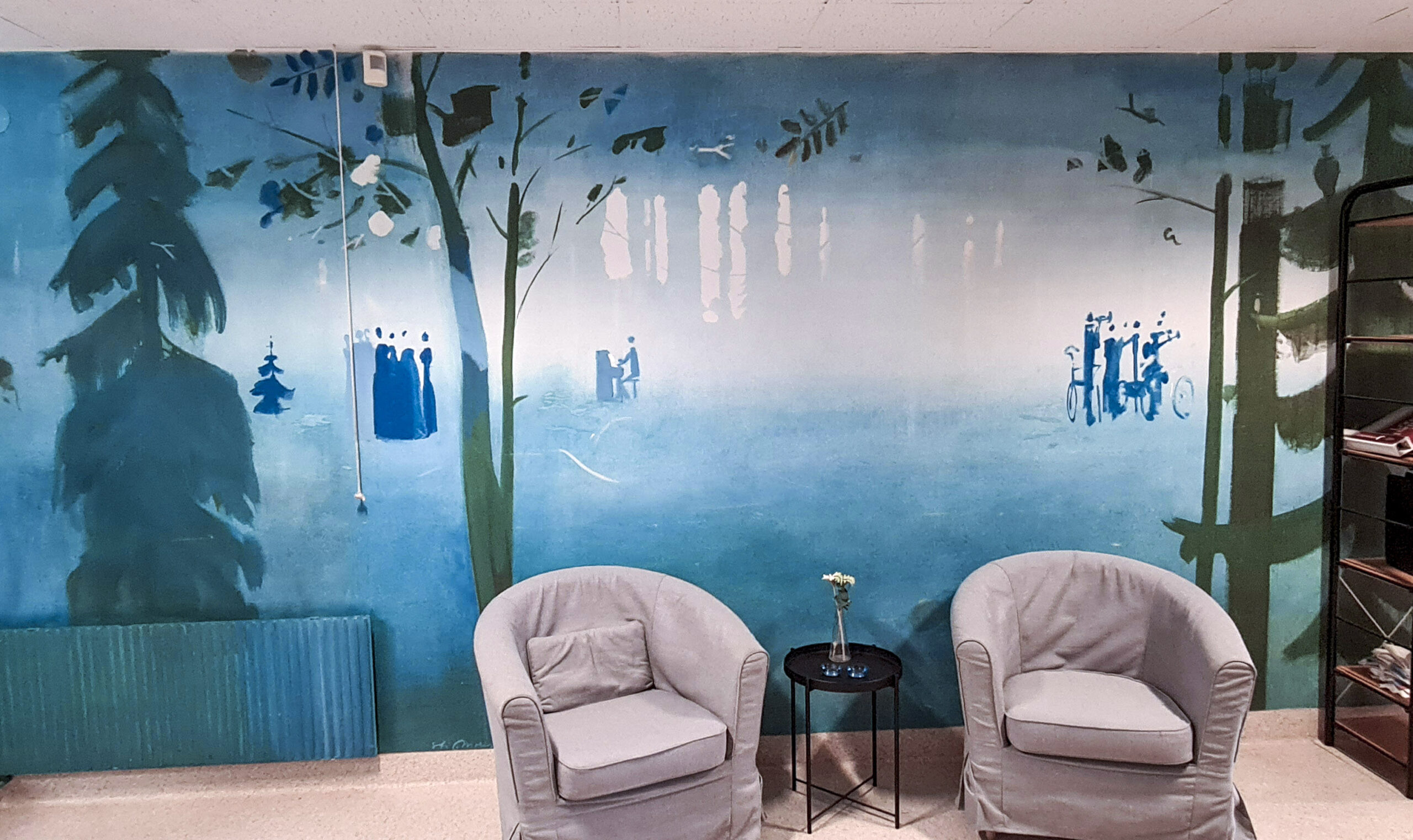 Interiör med stolar en bokhylla och väggmålning.