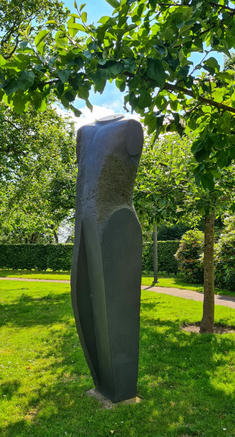 Skulptur i svart sten i sommarträdgård.