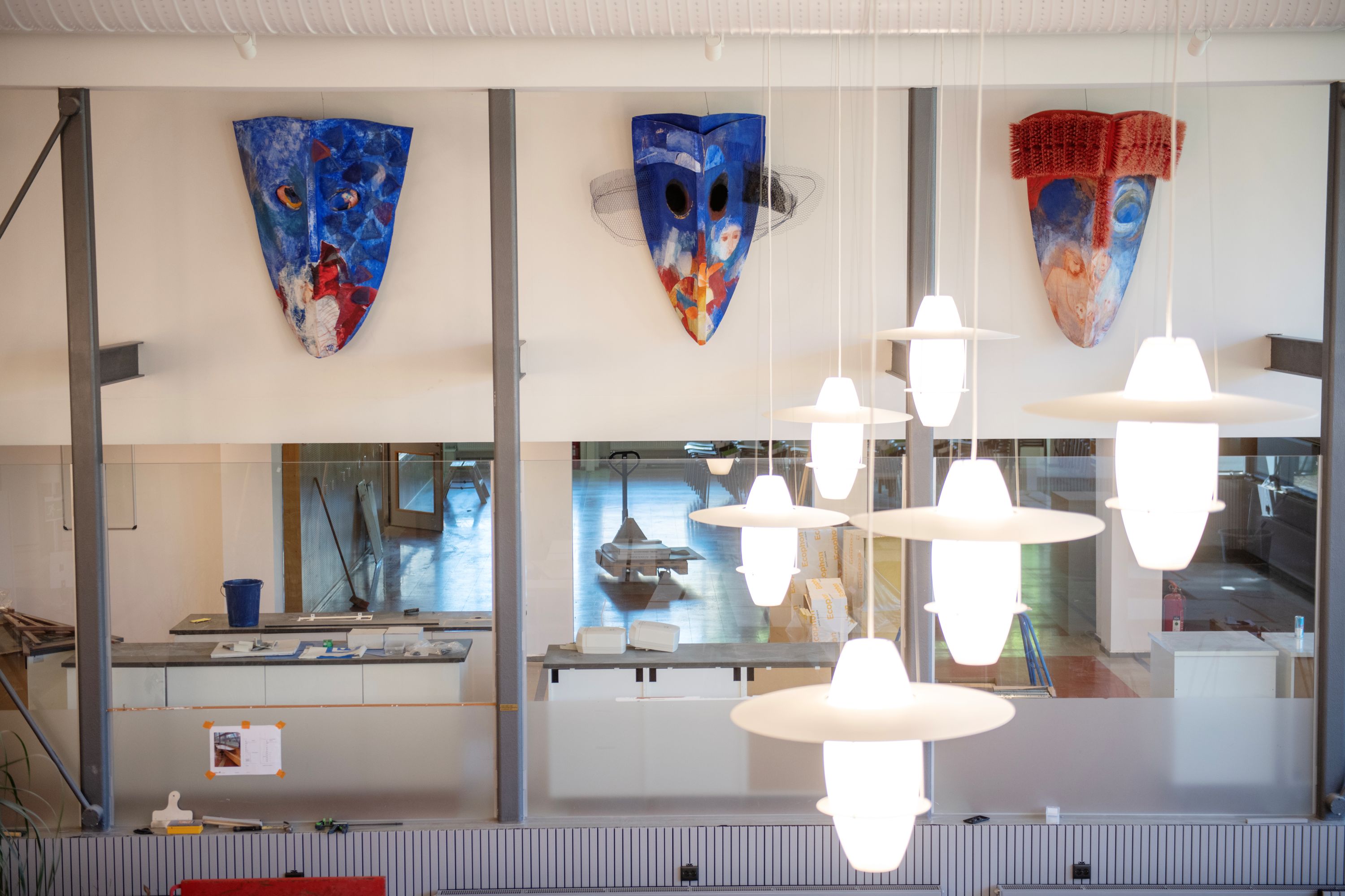 Interiör med tre stora masker i mörkt blå, röd och vit. 