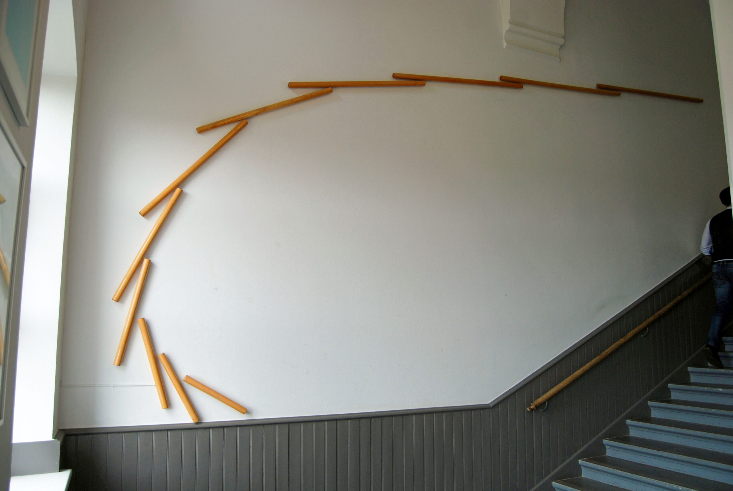 Vit vägg i trapphall med trästavar som formar en båge.