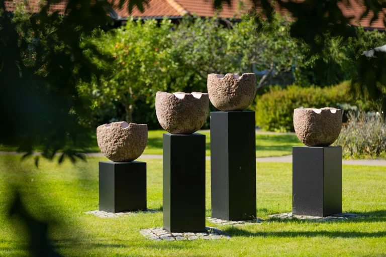 Utomhusbild om sommaren med blomformer i sten ovanpå svarta socklar av varierande höjd.