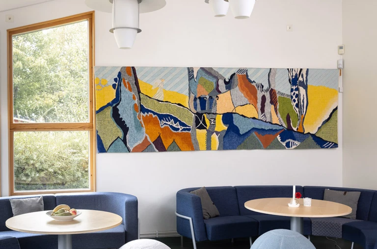 Interiör med väggtextil i abstrakta former, En liten ängel syns gå längs en linje.