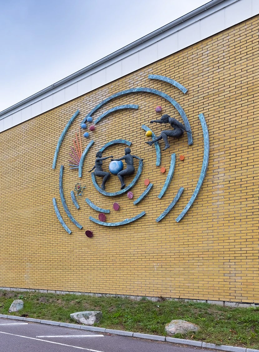 Väggkonstverk med koncentriska cirklar där tre människor, bollar och stavar verkar röra sig.